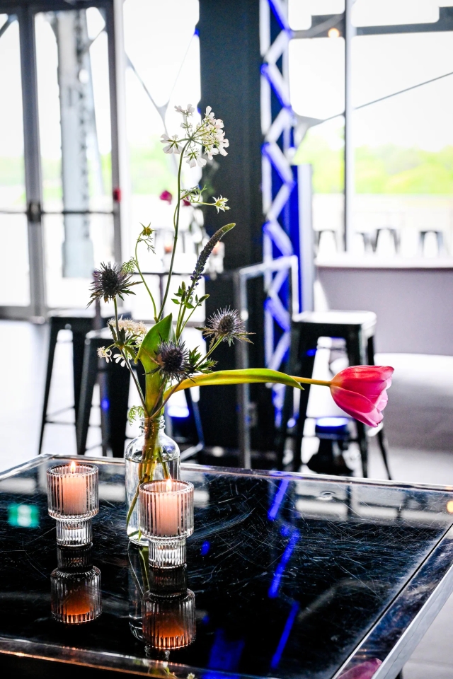 Two candles and a tall white and green floral arrangement atop a high black table.