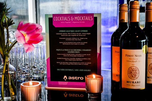 Cocktail and mocktail menu atop a black bar adorned with florals, candles, and wine bottes.