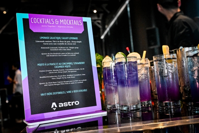 Closeup of cocktail and mocktail menu with purple cocktails in tall glasses off to the right.