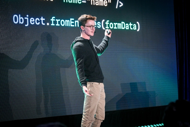 Ben Holmes on stage in front of a slide with a slide depicting form data.