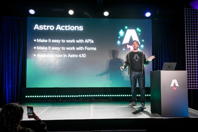 Fred K. Schott speaking on stage next to an Astro-branded podium. He is summarizing Astro Actions, which Ben Holmes just presented on.