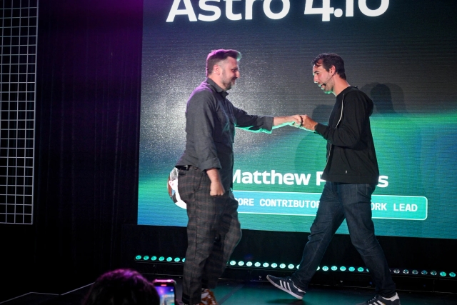 Fred K. Schott fist-bumps Matthew Phillips as he heads off stage and Matthew heads on stage to speak next.