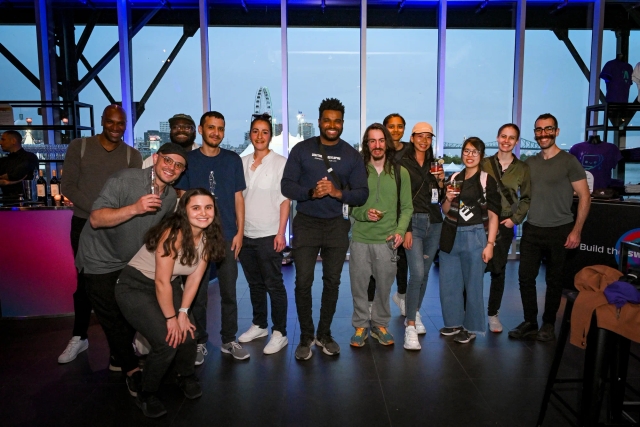 A large group of guests pose for a group photo in front of floor-to-ceiling windows.