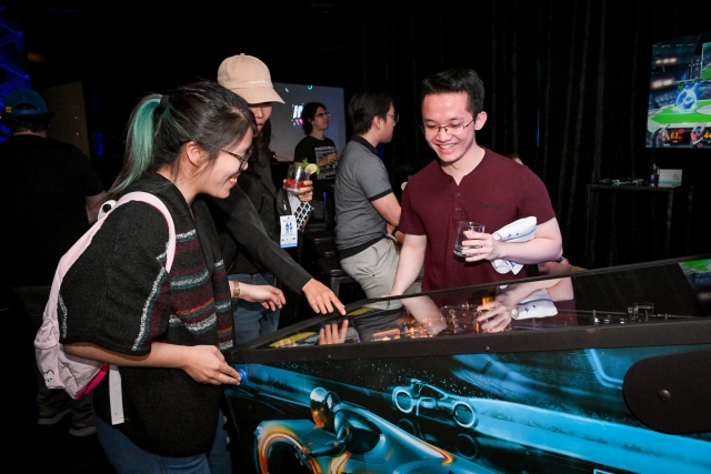 Guests smiling as they play pinball.